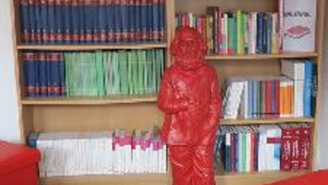 (Zwei große Bücherregale gefüllt mit diversen Büchern, im Vordergrund eine rote Karl-Marx-Figur)